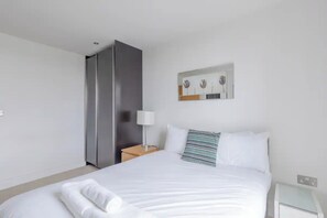 Ett hotellrum med en stor säng, ett nattduksbord med en lampa, ett konstverk som hänger på väggen och en garderob.