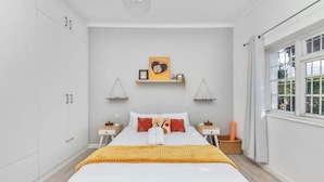 Une chambre moderne avec un grand lit, des murs blancs, une fenêtre avec des rideaux et une étagère ornée d’objets décoratifs.
