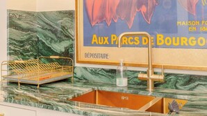 Un baño con encimera de mármol, un lavabo dorado y un póster antiguo que anuncia 'Ménetrel' en la pared.