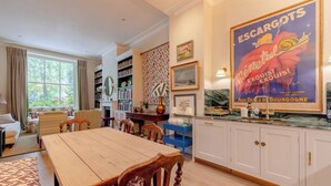 Una habitación bien iluminada con una mesa de comedor de madera, estanterías y un cartel grande en la pared.