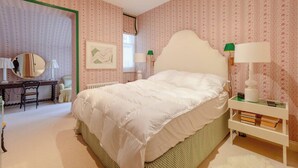 Un dormitorio con cama, mesitas de noche, un escritorio con silla, un espejo y un radiador.