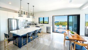 Een moderne keuken met een centraal kookeiland, barkrukken en een eettafel met stoelen.