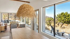 Een ruime kamer met een grote houten tafel, comfortabele zitmogelijkheden en grote ramen met uitzicht op een woestijnlandschap.