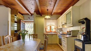 Een keuken met houten balken, een eettafel met stoelen, een bloevas en een fornuis.
