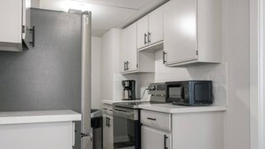 A modern kitchen with white cabinetry, a stainless steel refrigerator, a microwave, and a coffee maker.