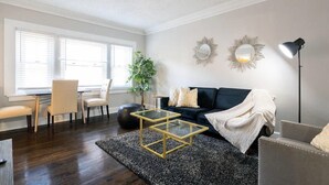 A living room with a dark wood floor, a black sofa, a glass coffee table, a round mirror, and a floor lamp.