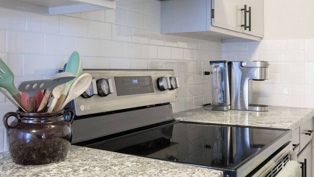 A kitchen with white cabinets, a stainless steel stove, and a coffee maker.