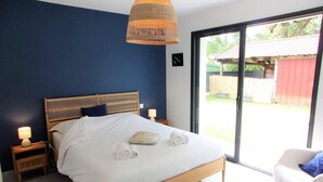 A bedroom with a wooden bed, white linens, a woven light fixture, and a view through a glass door to the outside.