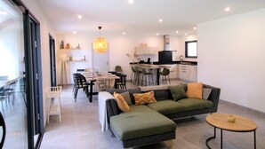 A modern living room with a sectional sofa, a dining area with a table and chairs, and a kitchen in the background.
