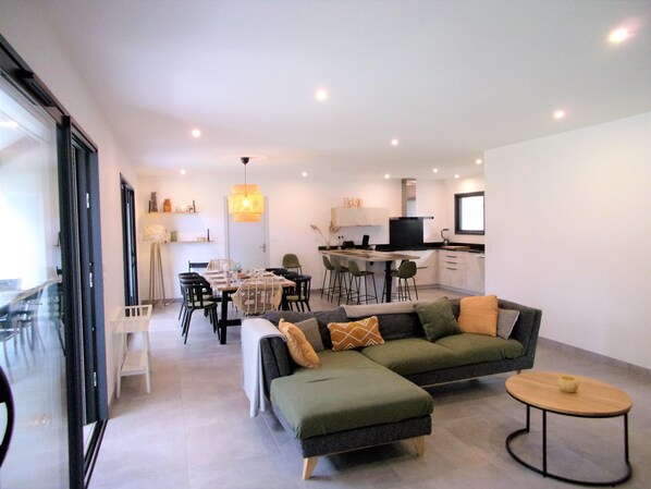 Una sala de estar moderna con un sofá modular, un comedor con mesa y sillas, y una cocina al fondo.