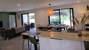 A modern kitchen with a central island, dining area with chairs, and a large sliding glass door leading to an outdoor patio.
