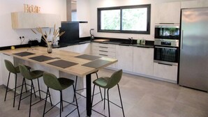A modern kitchen with a central island, bar stools, a built-in oven, and a window providing natural light.