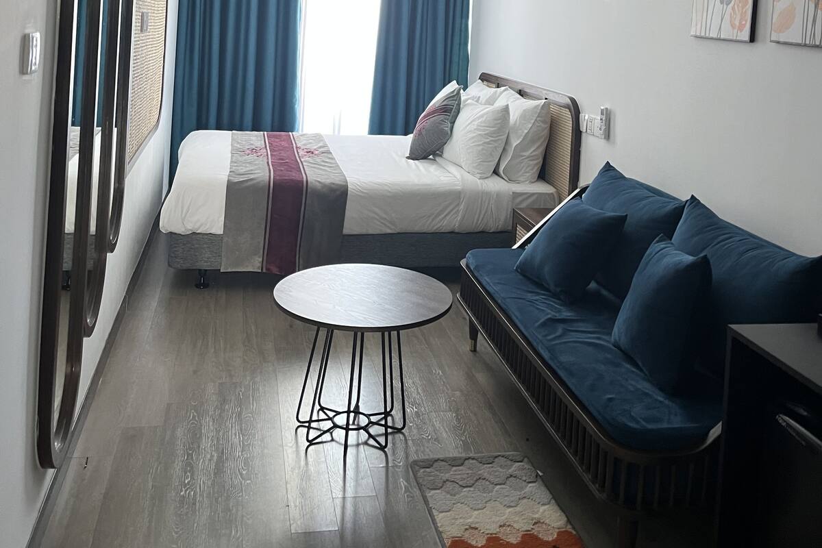 Ein modernes Hotelzimmer mit Bett, einer Couch, einem kleinen runden Tisch und einem großen Fenster mit Vorhängen.