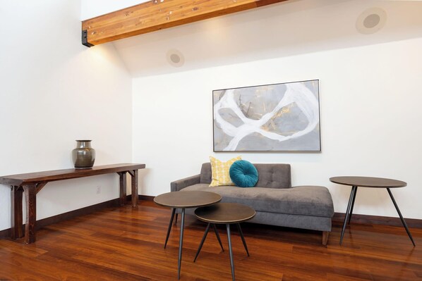 A modern living room with a grey sofa, two round tables, a wooden bench, and a large abstract painting on the wall.