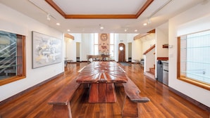 Una habitación amplia con una gran mesa de madera y bancos, una escalera y una zona de cocina.