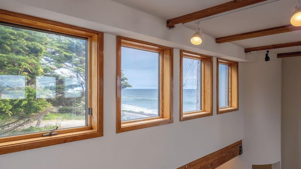 Una escalera con vigas de madera y ventanas amplias con vistas a la playa.