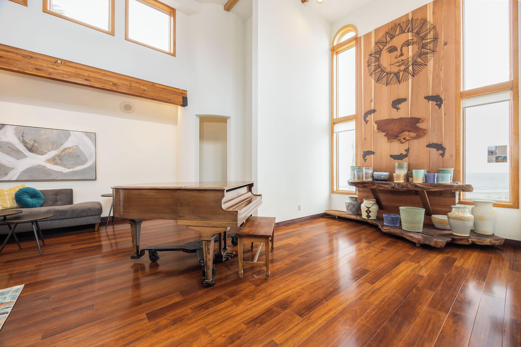 A spacious room with a grand piano, wooden shelves with decorative items, and a large window with a view.