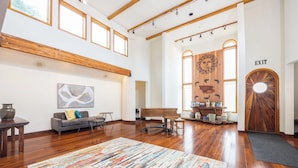 Una habitación amplia con pisos de madera, un piano, un sofá y un ventanal grande.