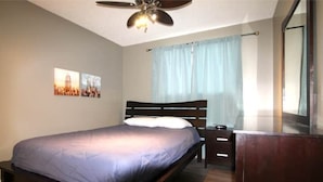 Ein Schlafzimmer mit Bett, Holz-Kopfteil, Nachttisch, Kommode und Deckenventilator.