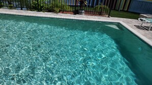 Ein klarer Swimmingpool mit einer gefliesten Umrandung und einem umgebenden Zaun.
