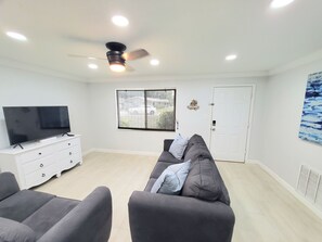 A modern living room with a flat-screen TV, grey sofas, a white dresser, and a ceiling fan.