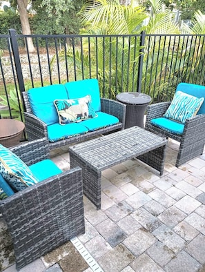 Outdoor wicker furniture with blue cushions, a round table, and a metal fence in the background.