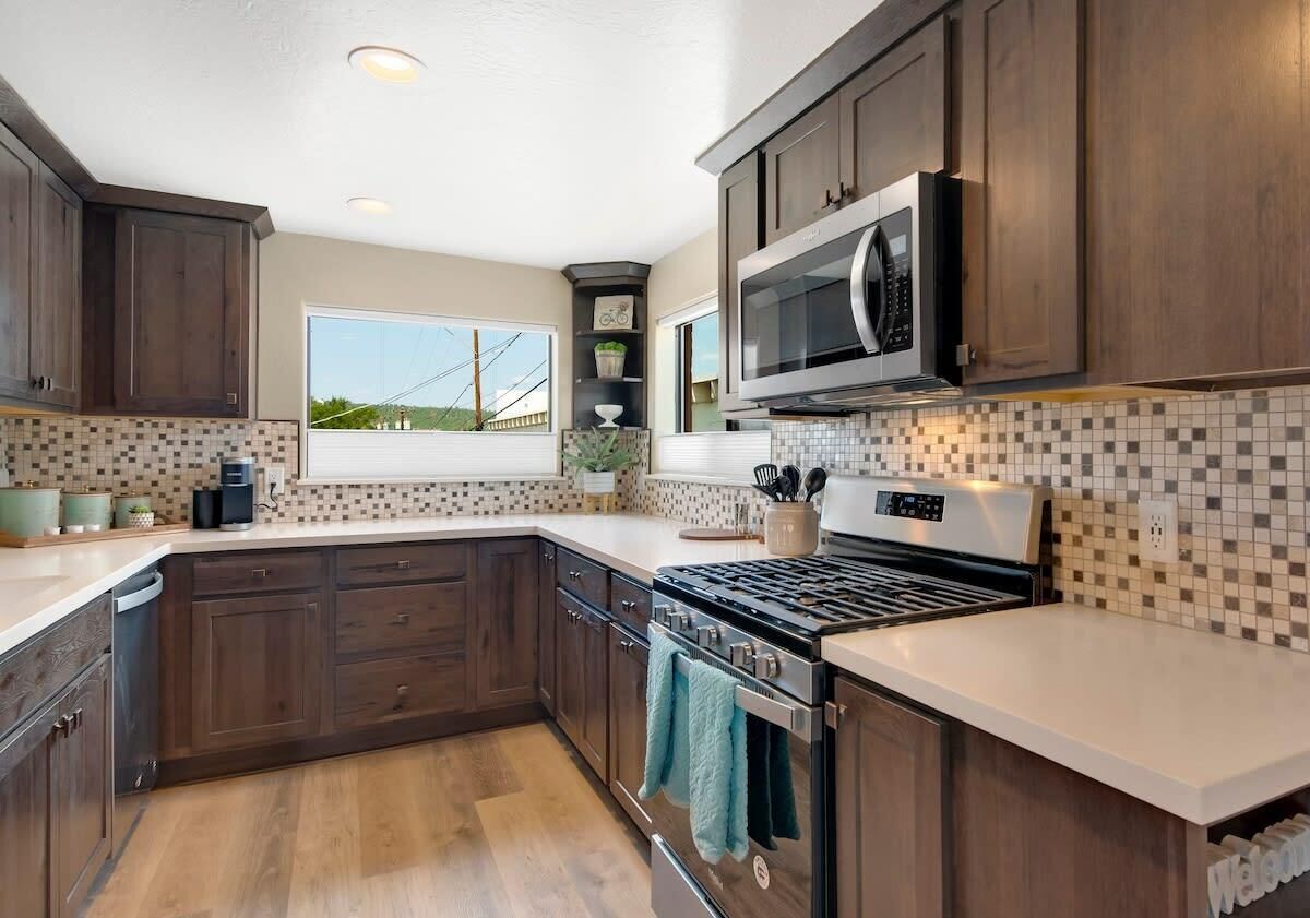 A modern kitchen with dark wooden cabinets, a large microwave, a stove, and a tiled backsplash.