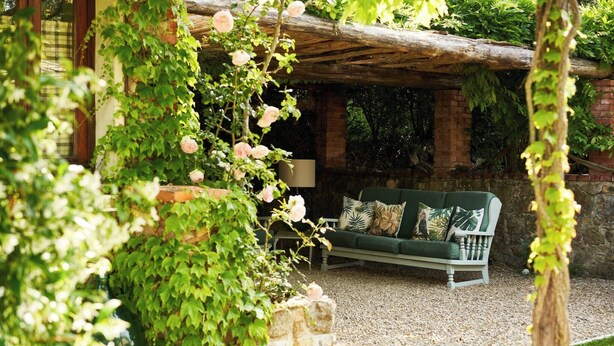 A cozy outdoor seating area with a green sofa and cushions, surrounded by lush greenery and a stone planter. - La Vignaccia the Old Barn - Villa W Private Pool (Pergine Valdarno)