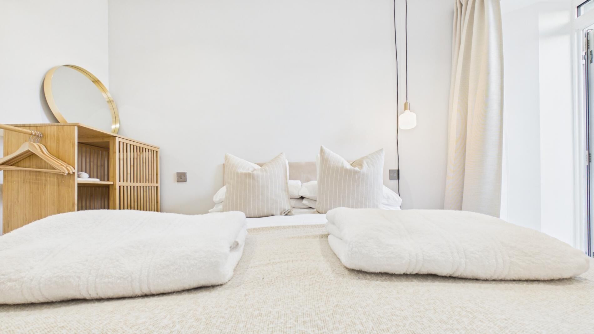 A minimalist bedroom with a bed, pillows, a wooden wardrobe, and a hanging light fixture.