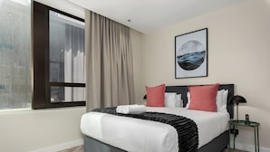 Een moderne hotelkamer met een groot bed, uitzicht op de stad door een raam en een ingelijste afbeelding aan de muur.