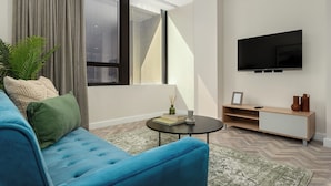 Een moderne woonkamer met een blauwe bank, een salontafel, een aan de muur bevestigde televisie en een groot raam met gordijnen.