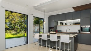 Eine moderne Küche mit einer großen Kochinsel, Barhocker und Blick auf einen Garten durch Glastüren.