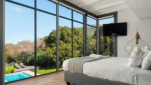 Ein Schlafzimmer mit großem Fenster, einem Bett, einem Fernseher und einer Pendelleuchte.