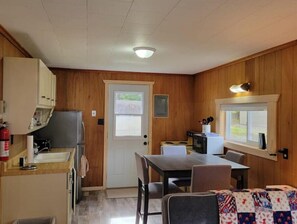 A compact kitchen with wooden walls, a refrigerator, a microwave, and a dining area with a table and chairs.