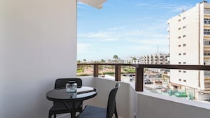 A balcony with a round table and chairs, overlooking a cityscape with buildings and palm trees.