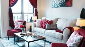 Una sala de estar con sofá, sillones, una mesa de centro y una ventana con cortinas.