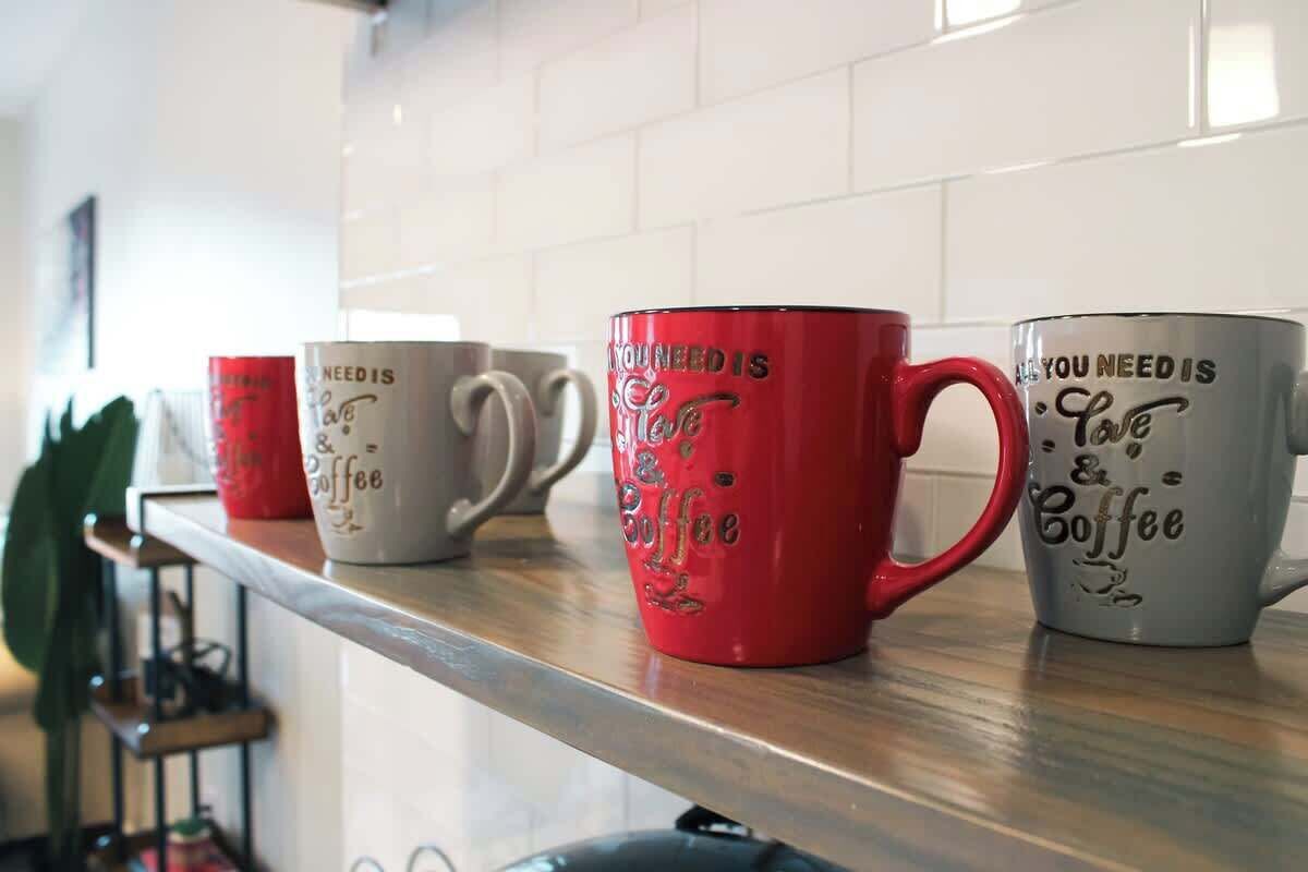 Une rangée de tasses à café sur une étagère, avec l’inscription : « Tout ce dont vous avez besoin, c’est de l’amour et du café. »