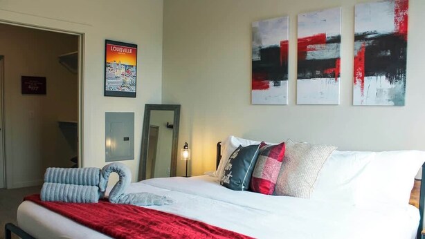 Habitación de hotel con una cama, una colcha roja, almohadas, un espejo y un cartel con una vista urbana.