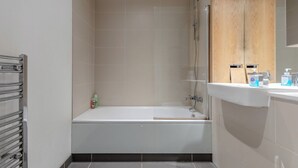 A bathroom with a bathtub, a shower, and a sink with toiletries. - Stylish One BDR Flat Close to Greenwich (London)