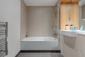 Ett badrum med badkar, dusch och handfat med tillhörande hygienartiklar.