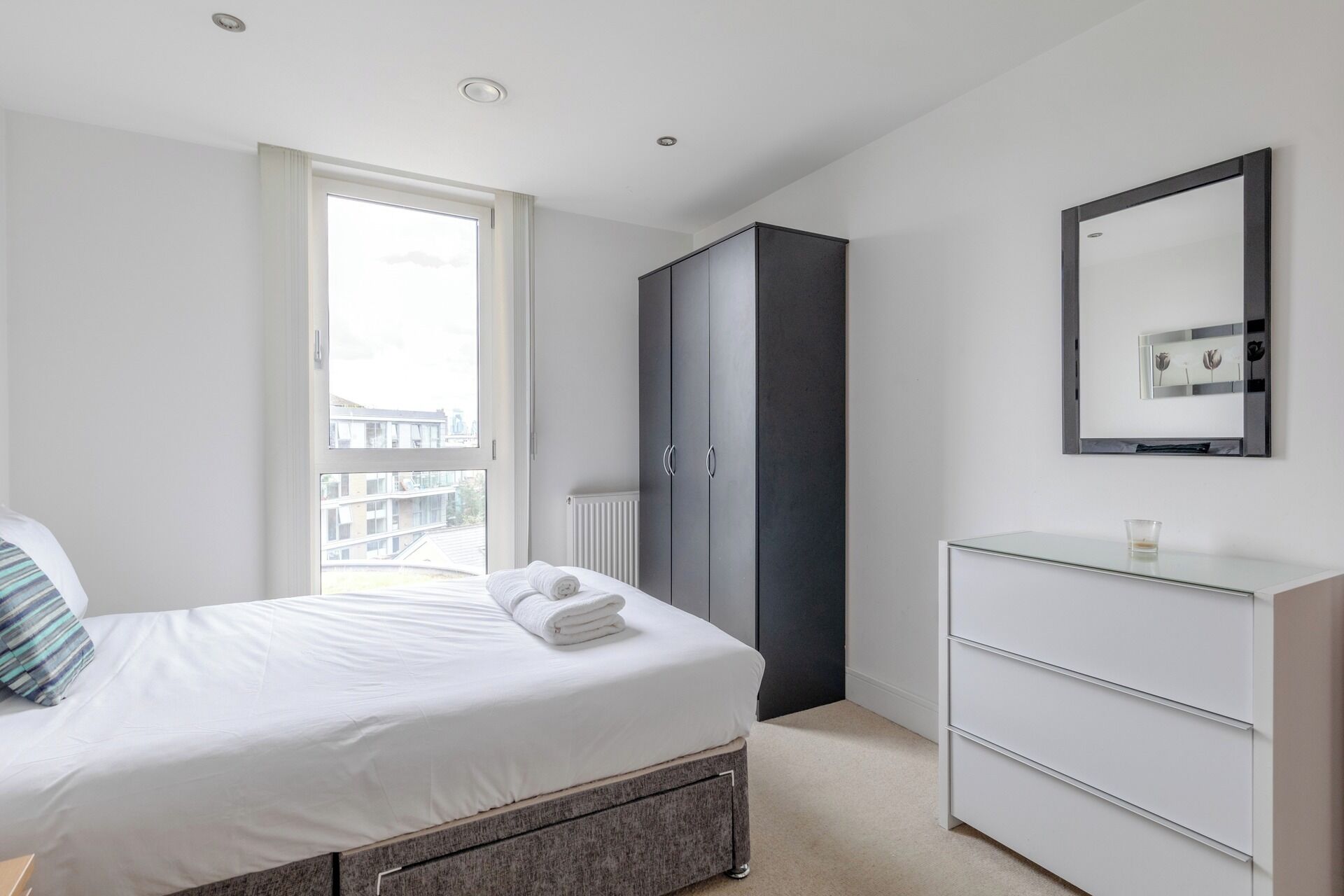 Een slaapkamer met een bed, een kledingkast, een dressoir en een groot raam.
