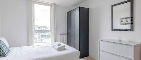 Een slaapkamer met een bed, een kledingkast, een dressoir en een groot raam.