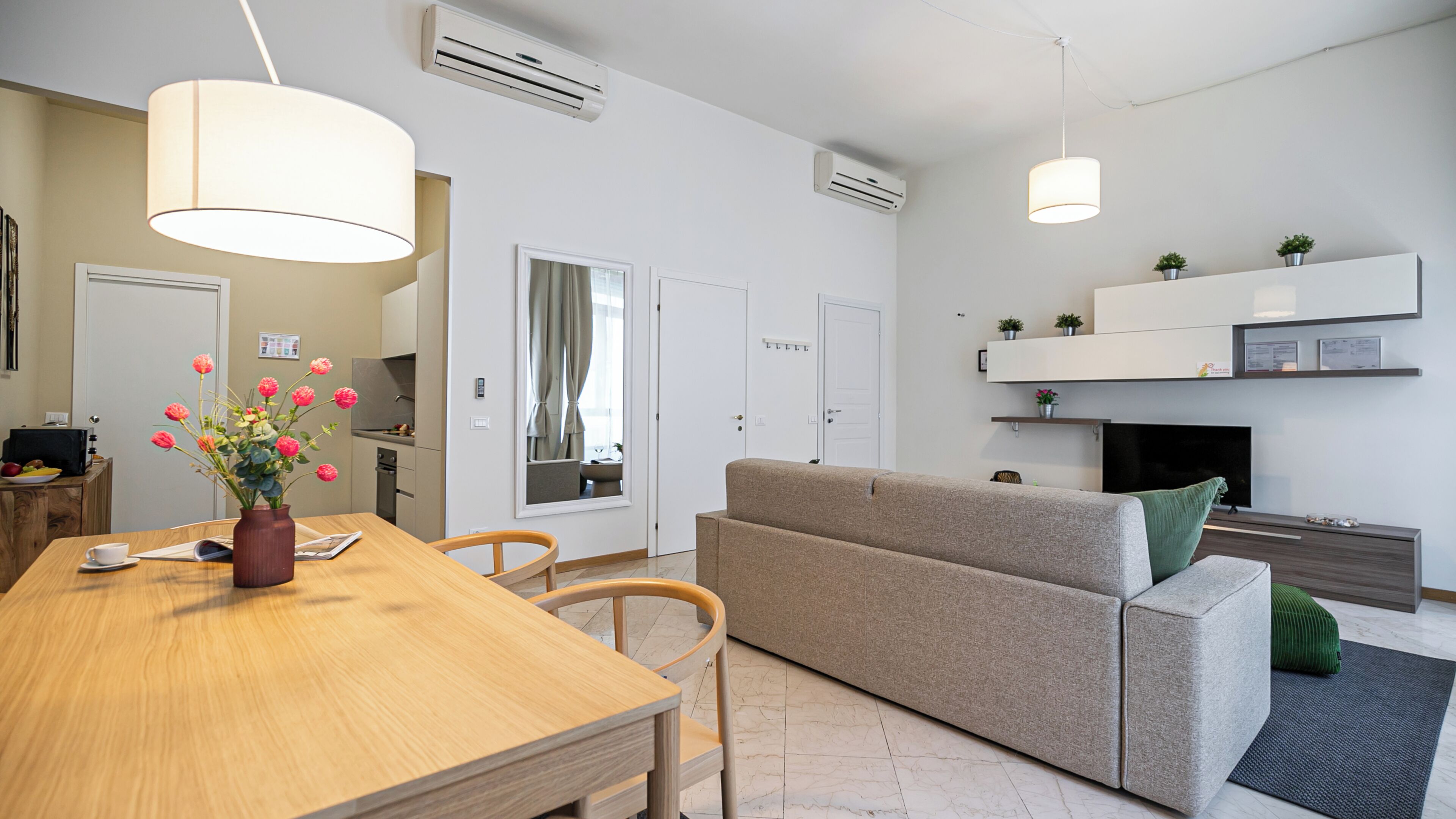 A modern living room with a sofa, a dining table with chairs, a kitchen area, and a fireplace.