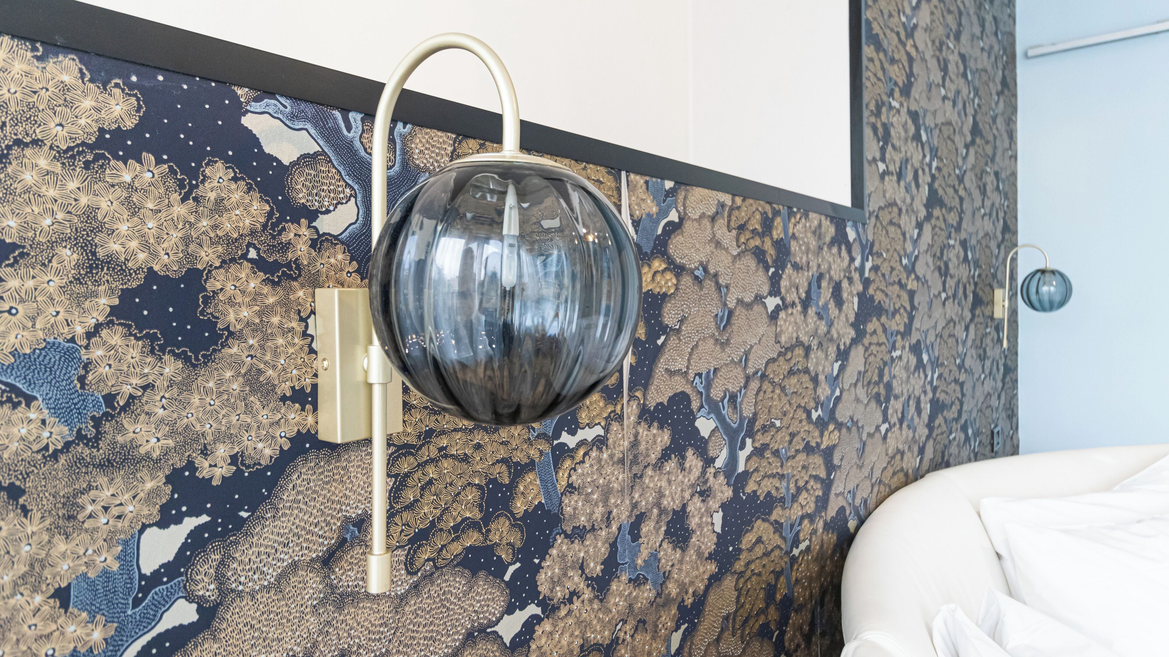 A modern room with a patterned wallpaper, a round mirror, and a white bed.