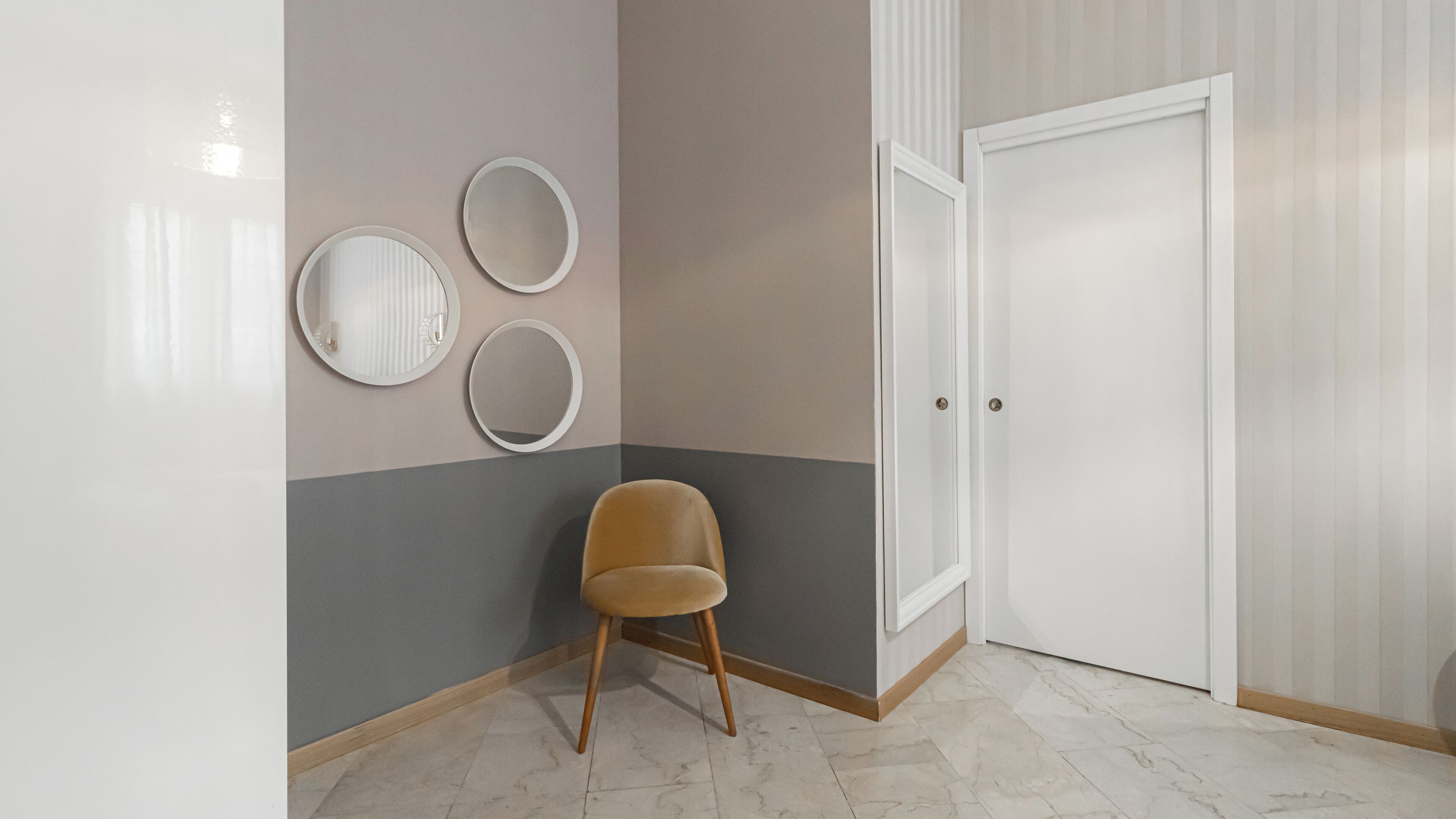 A corner room with a door, a chair, and three wall-mounted mirrors.