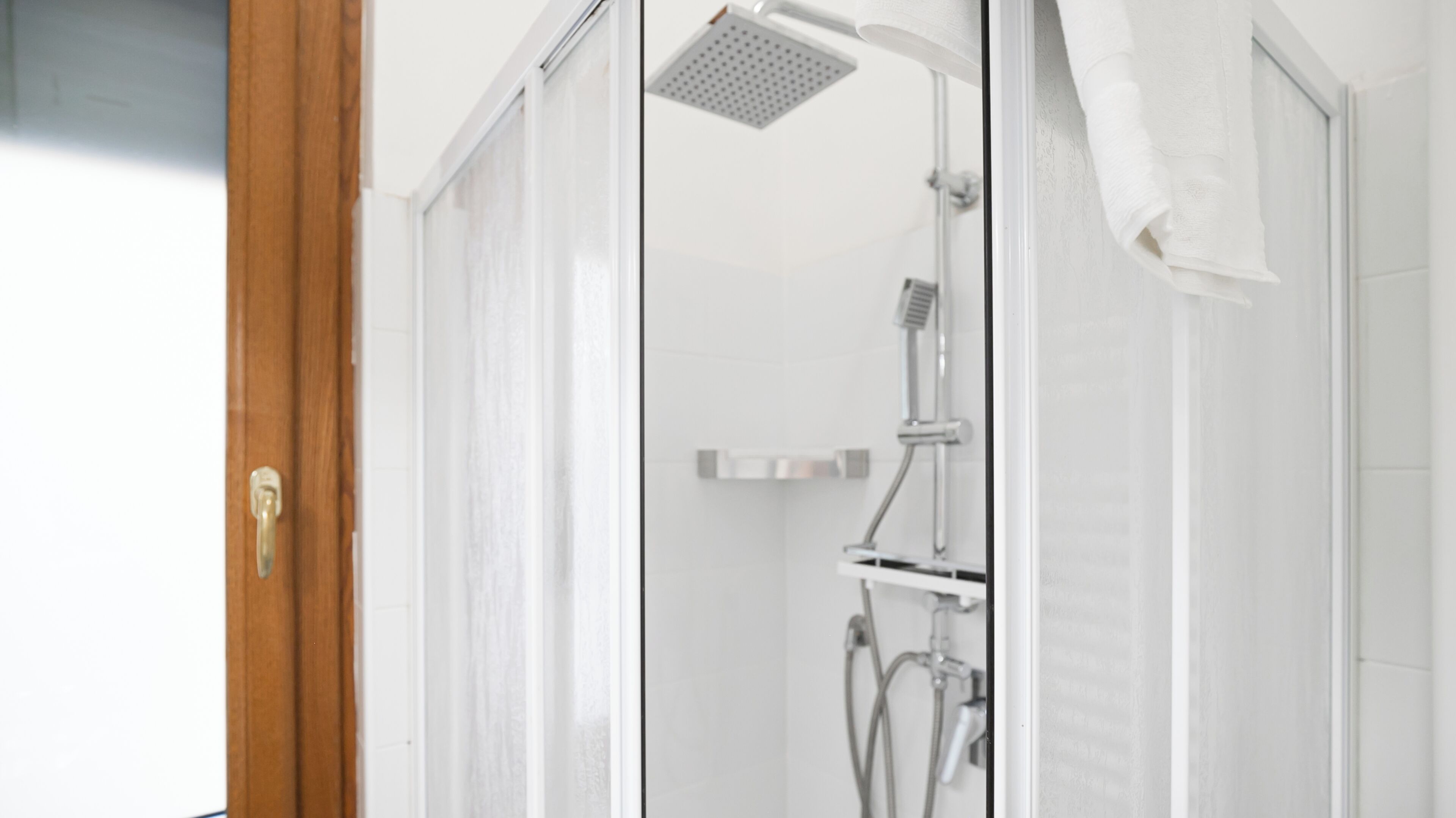A glass-enclosed shower with a handheld showerhead and a wall-mounted faucet.