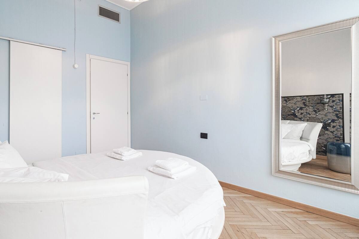 Ein modernes Schlafzimmer mit einem großen Bett, einem Spiegel und einem Holzboden im Fischgrätmuster.