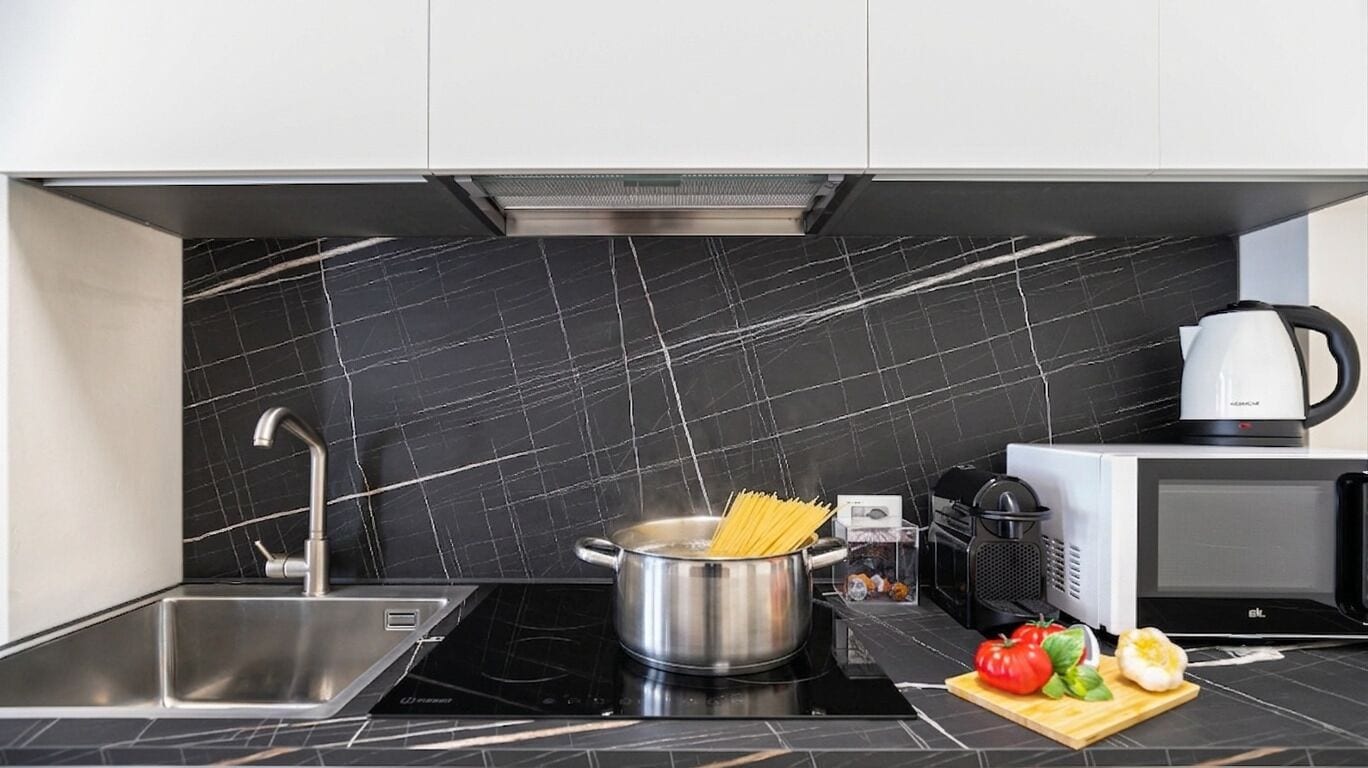 Cozinha moderna com painel de fundo de mármore preto, eletrodomésticos de aço inoxidável e tábua de corte com legumes.