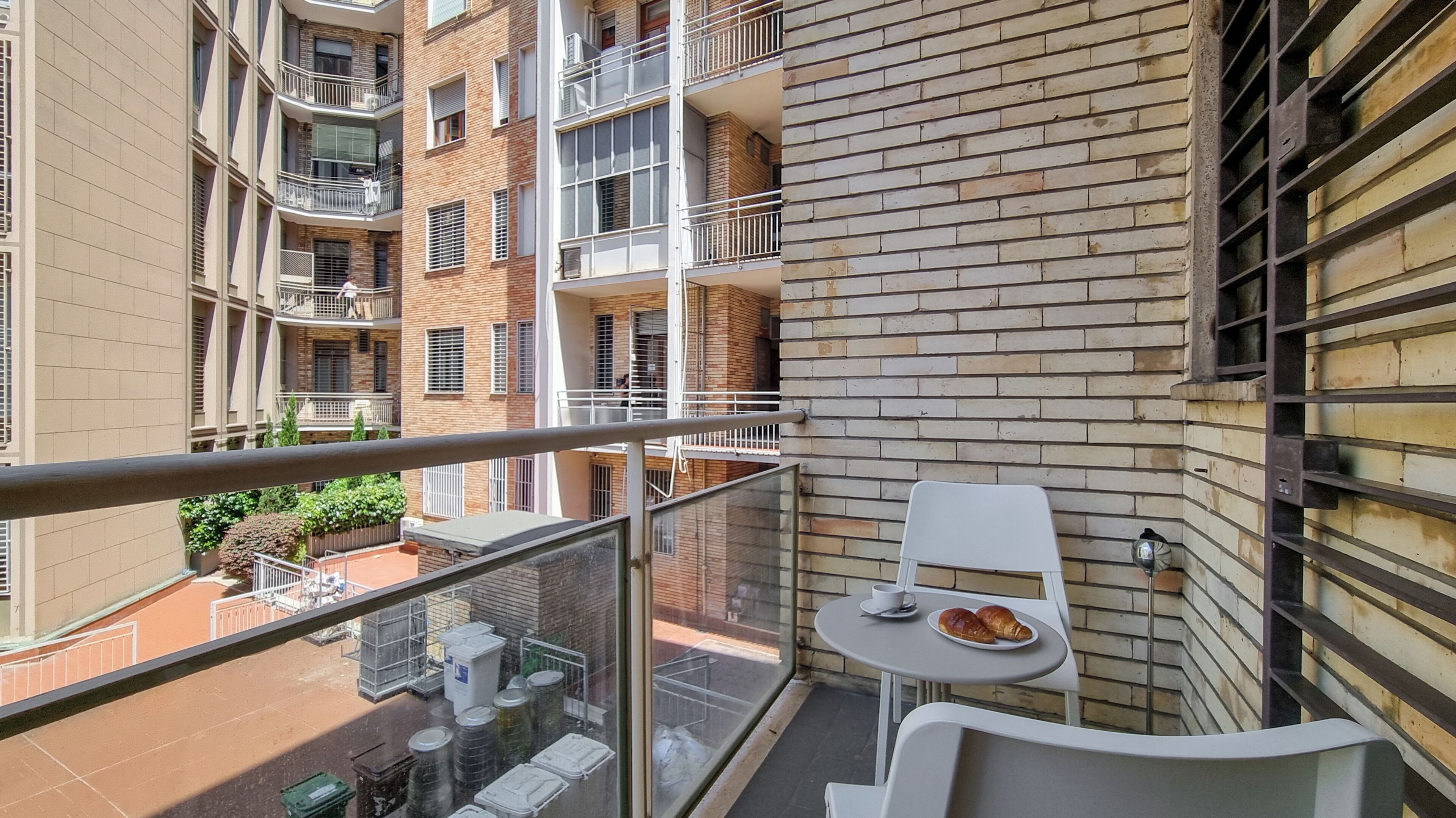 A balcony with a table and chairs, a plate with food, and a view of a brick building with balconies.