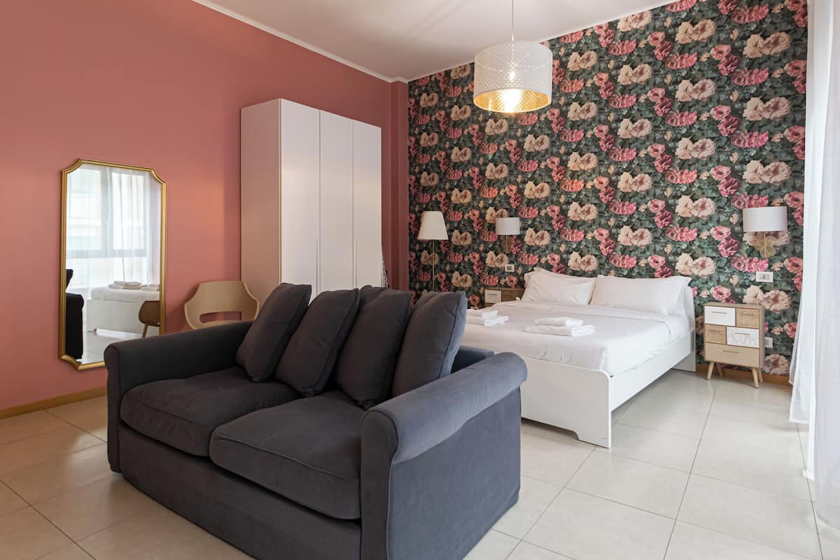 Ein modernes Schlafzimmer mit einer grauen Couch, einem weißen Bett und blumigem Wandpapier.
